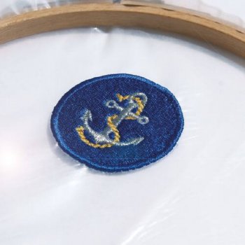 Ett heltäckande broderat emblem med ankarmotiv i en brodyrbåge, spänt direkt på den transparenta SOLVY FILM 80. Bilden visar hur