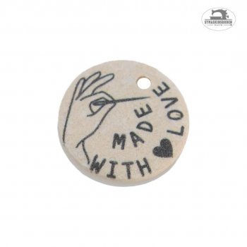 En fin vit applikationsknapp i återvunnen bomull med svart mönster av en hand som håller i en nål och texten made with love